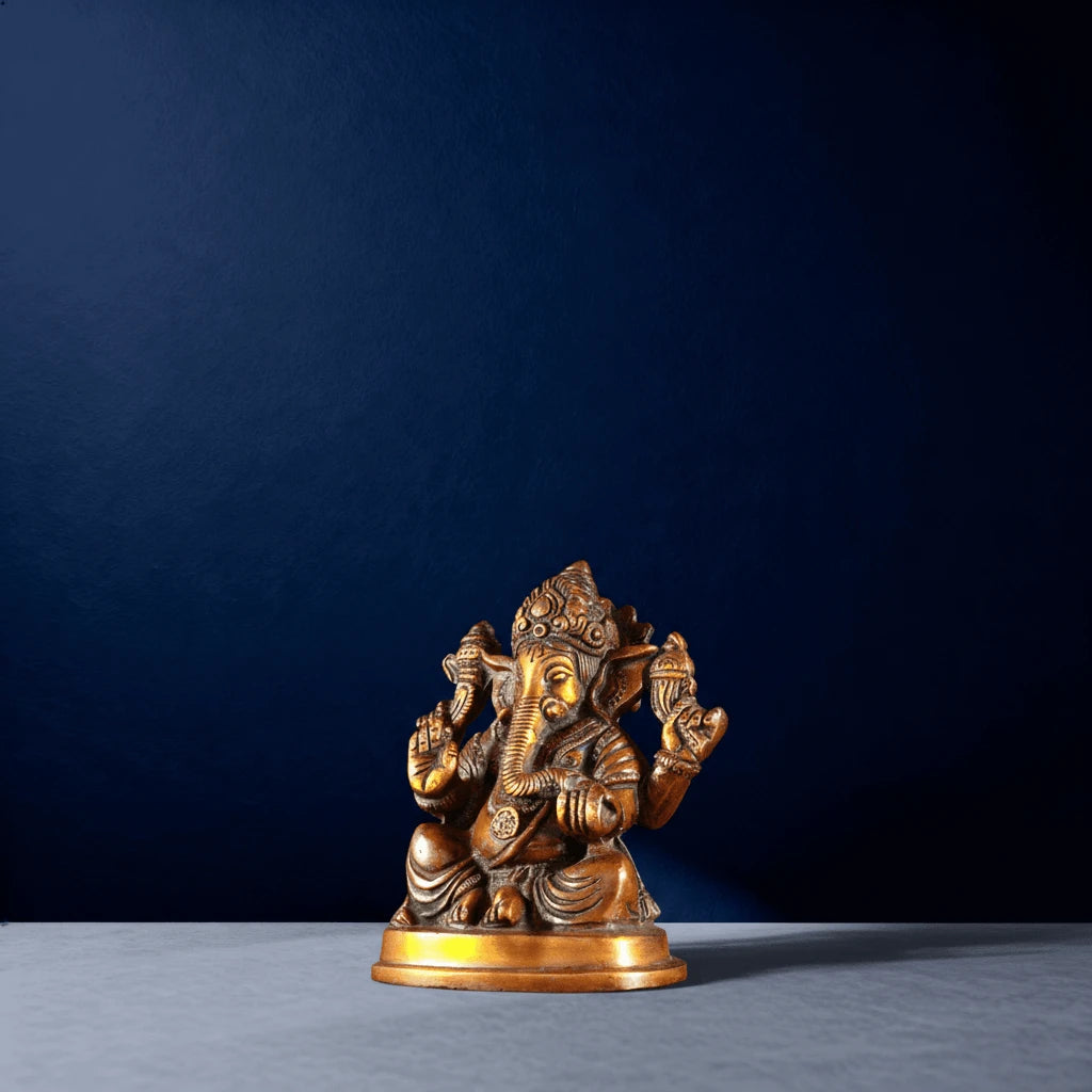 Side-angled shot of golden Ganesha figurine placed on a white tabletop with deep blue backdrop