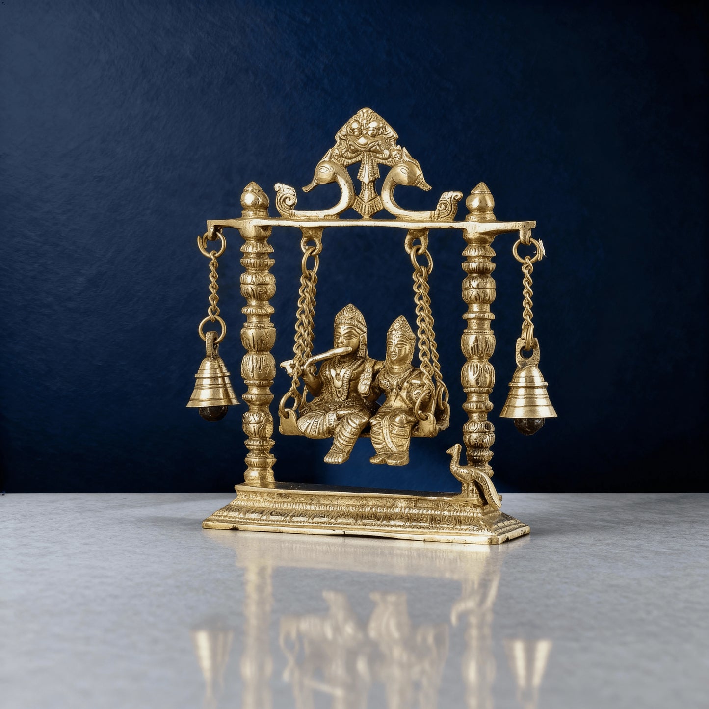 Handcrafted brass Radha Krishna jhula idol with detailed peacock arch and hanging bells, premium home decor showpiece.