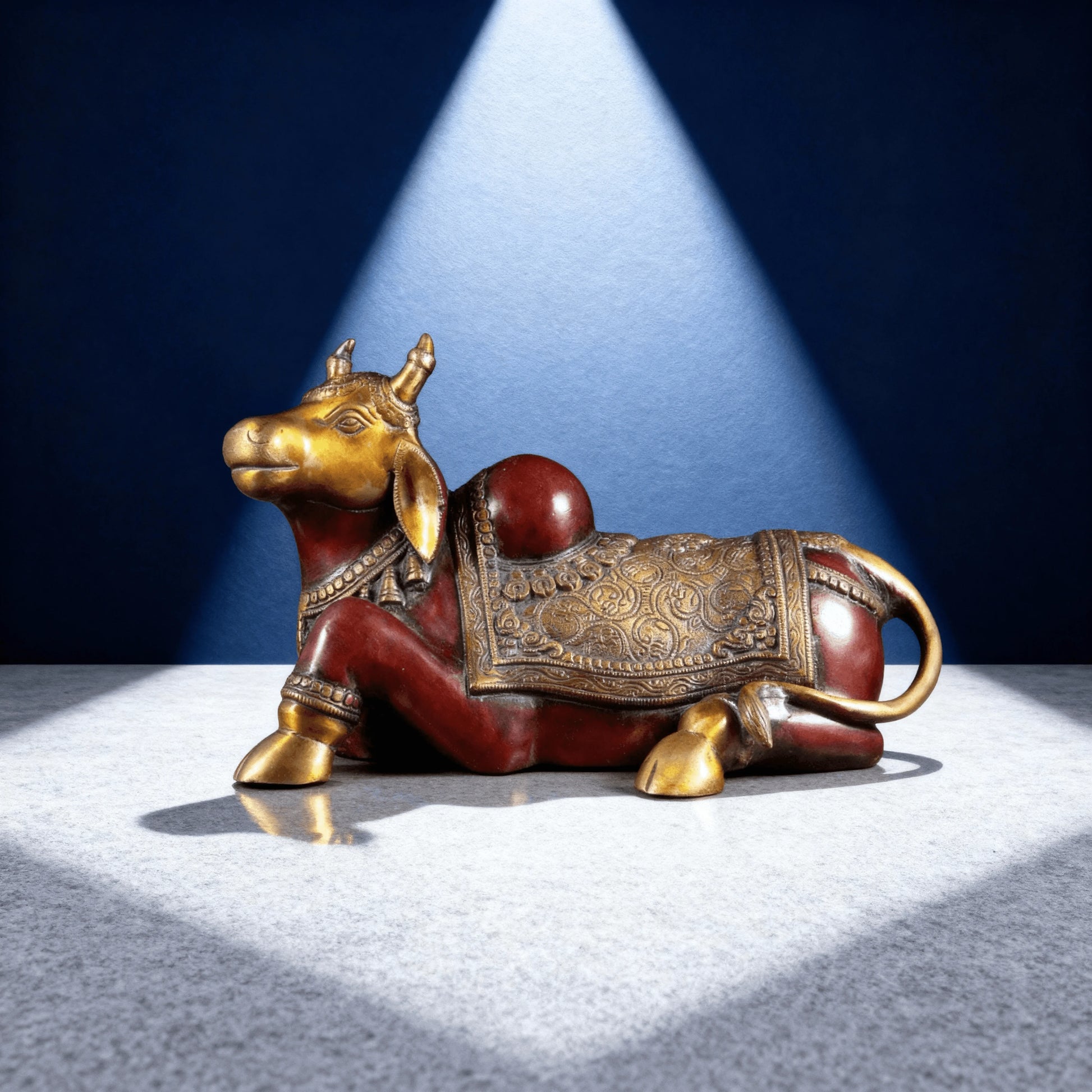 Side view of handcrafted red and gold Nandi idol with engraved saddle design
