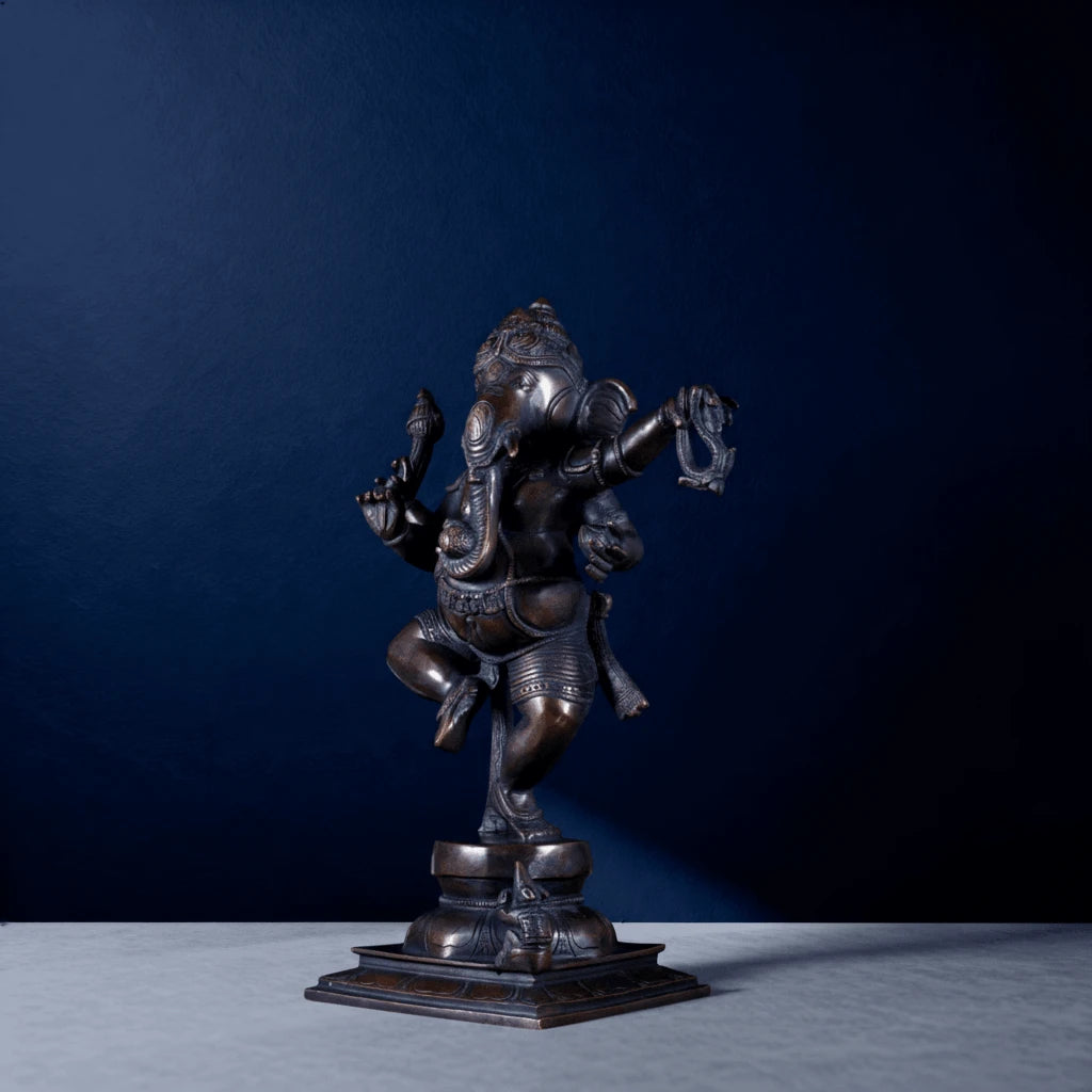 Side view of antique bronze dancing Ganesha statue in dynamic posture on decorative pedestal