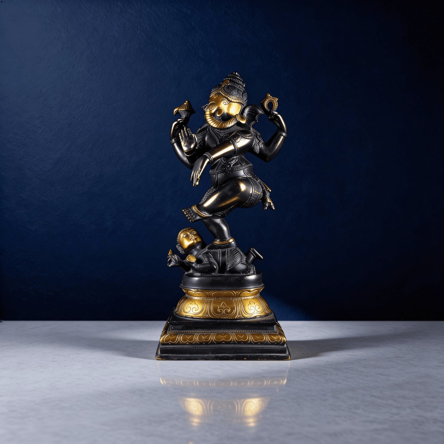 Front-facing black Ganesha idol with gold face and accents in dynamic dance pose on pedestal