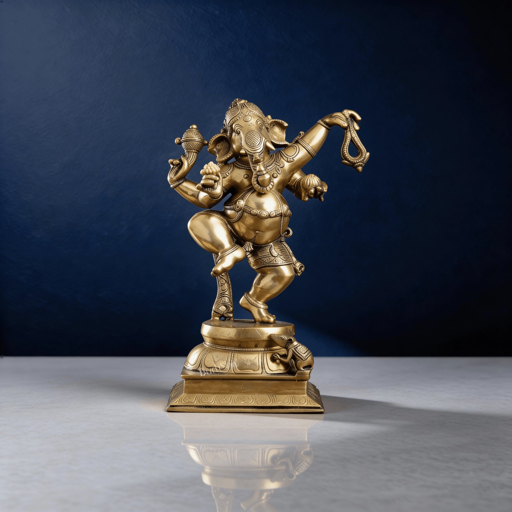 Front view of shiny brass Ganesha murti in dancing pose with detailed ornaments and mouse figure