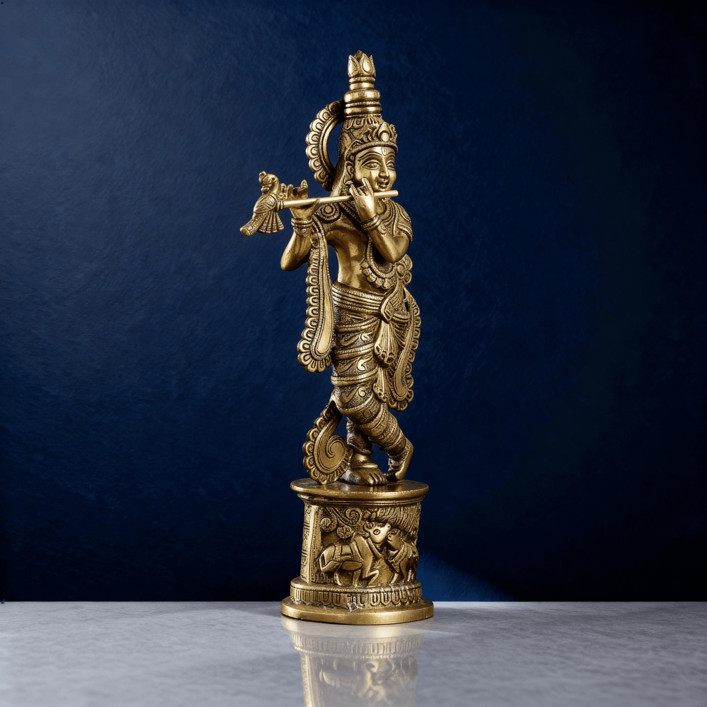 Pure brass Krishna flute statue on marble surface with detailed carvings and golden finish, photographed against a dark blue luxury background.