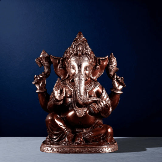 Front view of pure brass Ganesha statue with intricate detailing and four-arm design on a dark blue background