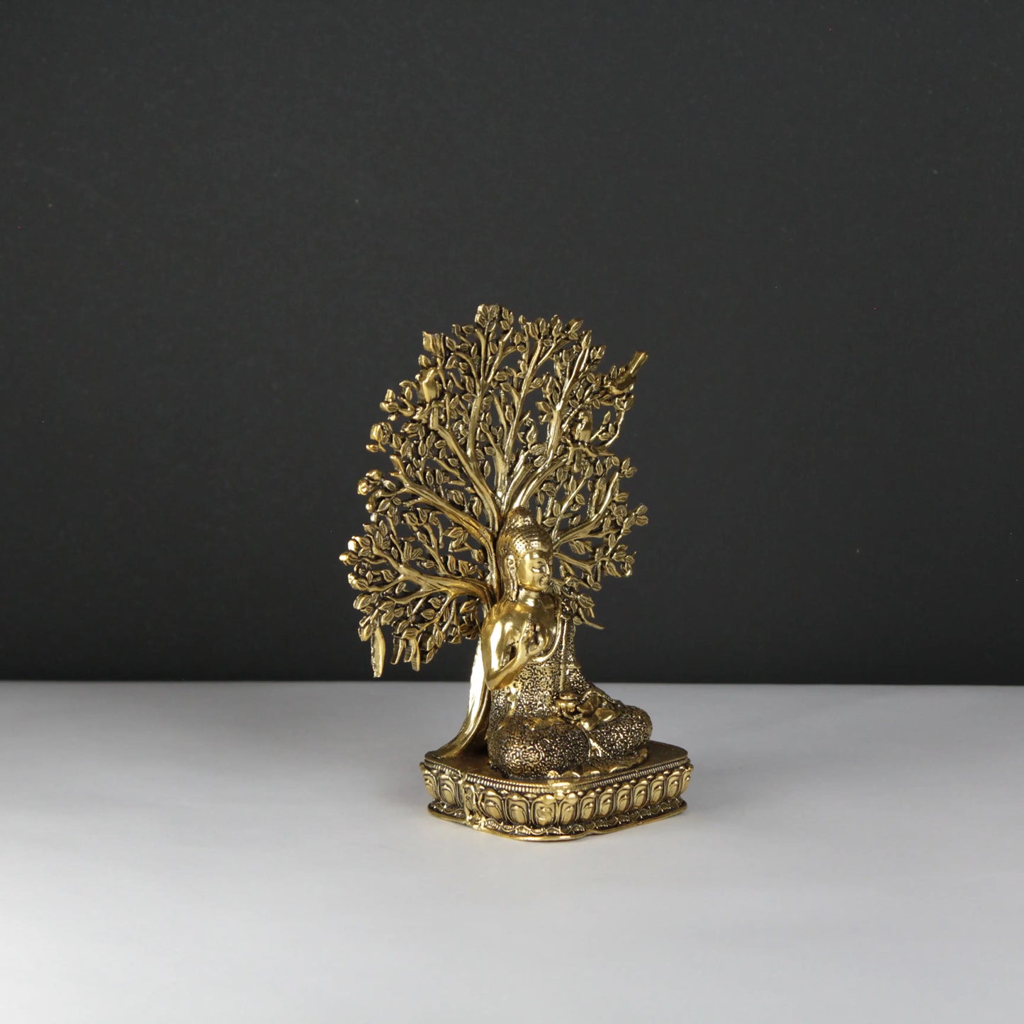 Buddha statue of a seated figure under a tree on a dark background