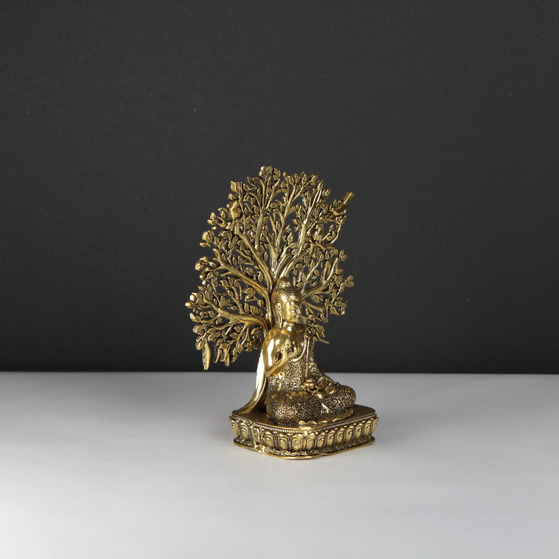 Buddha statue of a seated figure under a tree on a dark background