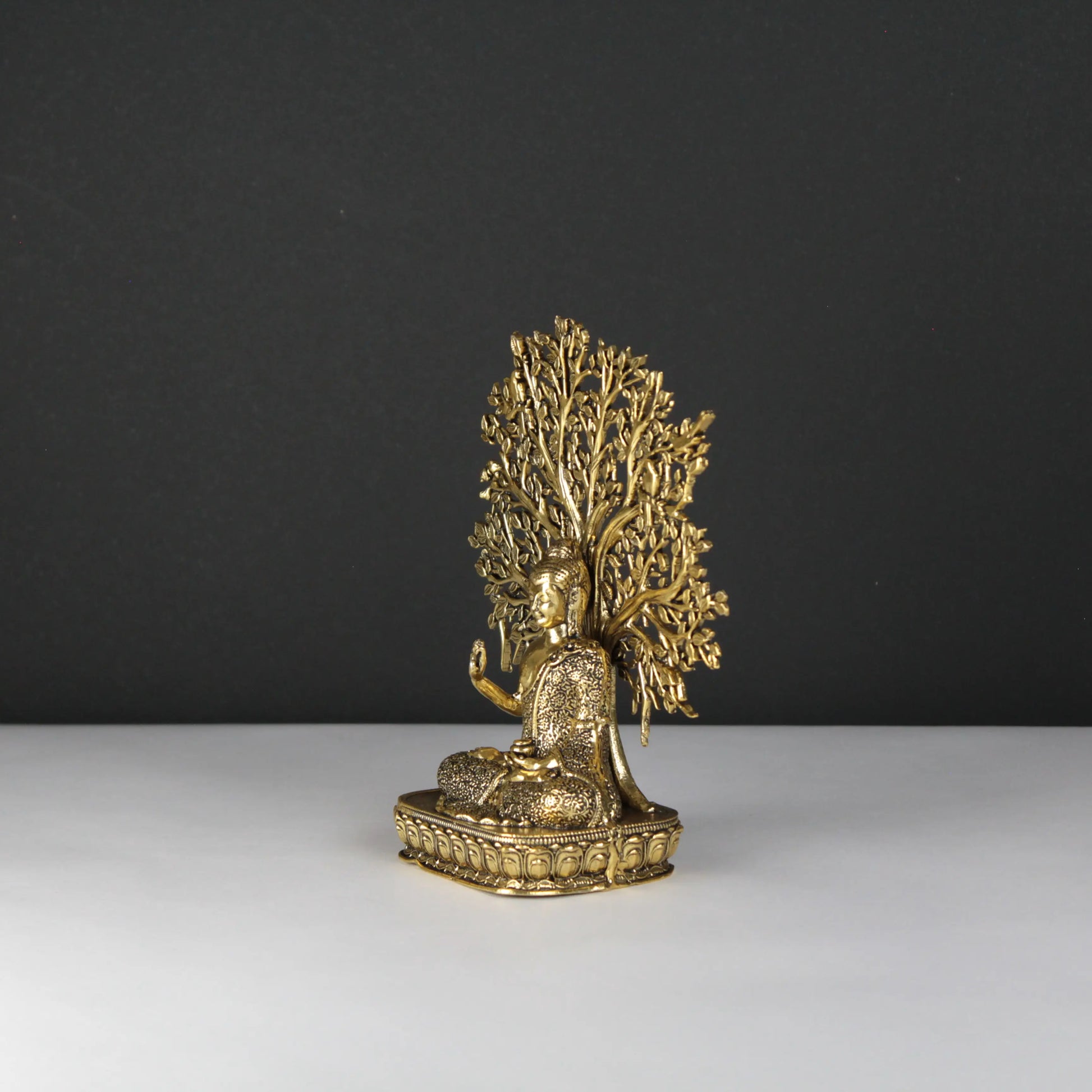 Gold Buddha statue of a seated figure with a tree-like headdress on a dark background