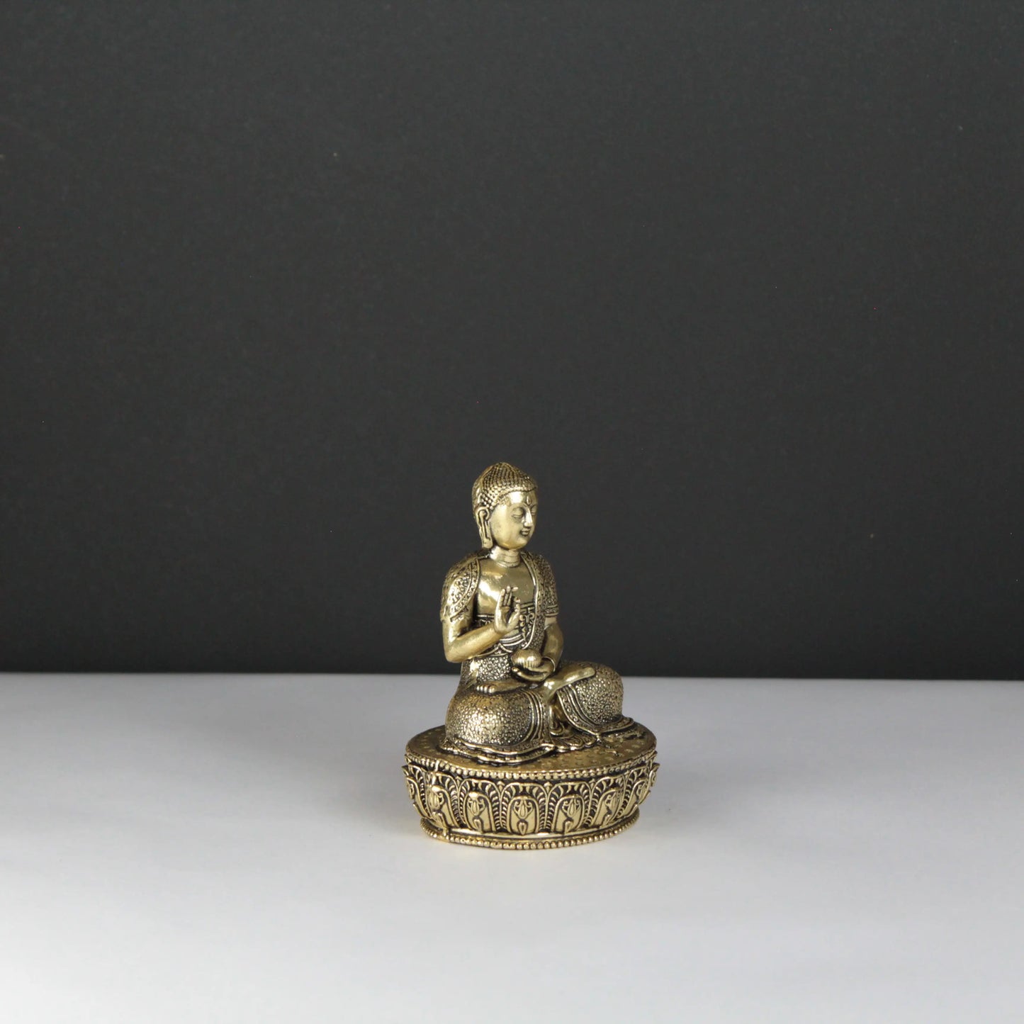 Brass Buddha statue on a white surface with a dark gray background