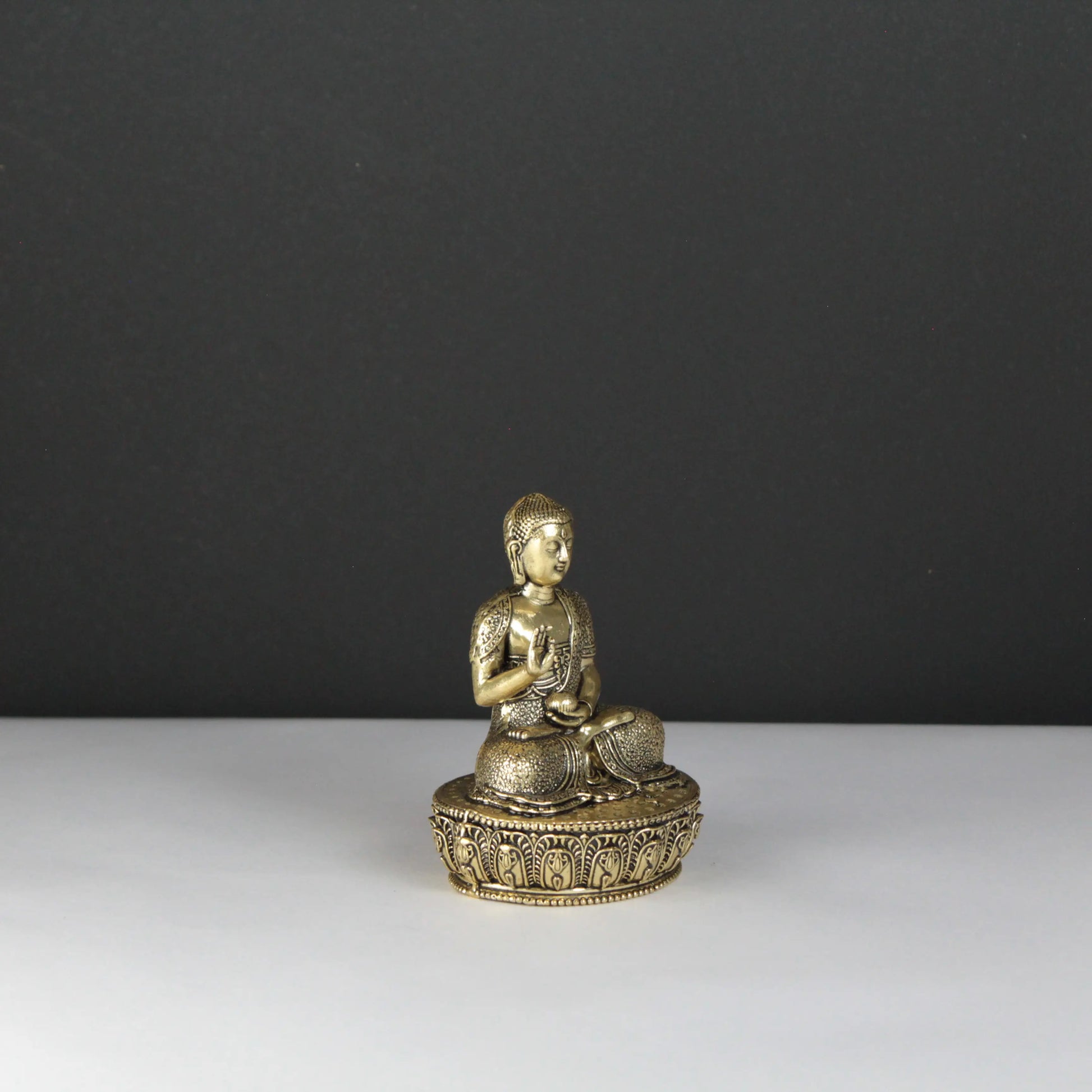 Brass Buddha statue on a white surface with a dark gray background