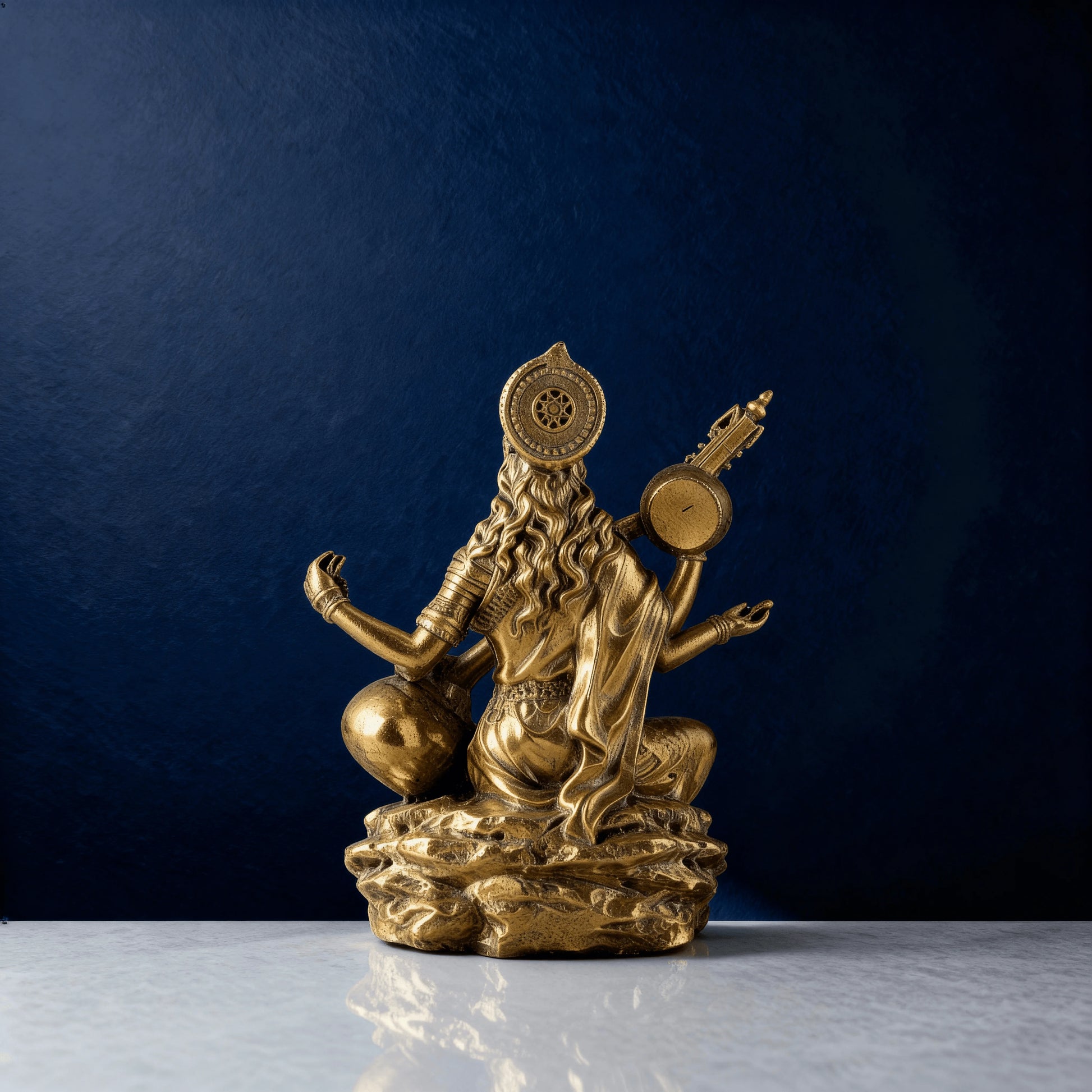 rear view of brass Saraswati idol highlighting the hair, draped clothing, and back details, photographed against a deep blue backdrop