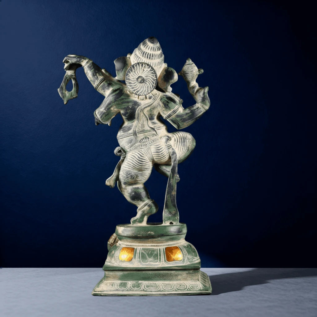 Back view of green dancing Ganapati statue showing carved robe patterns and glowing pedestal lights
