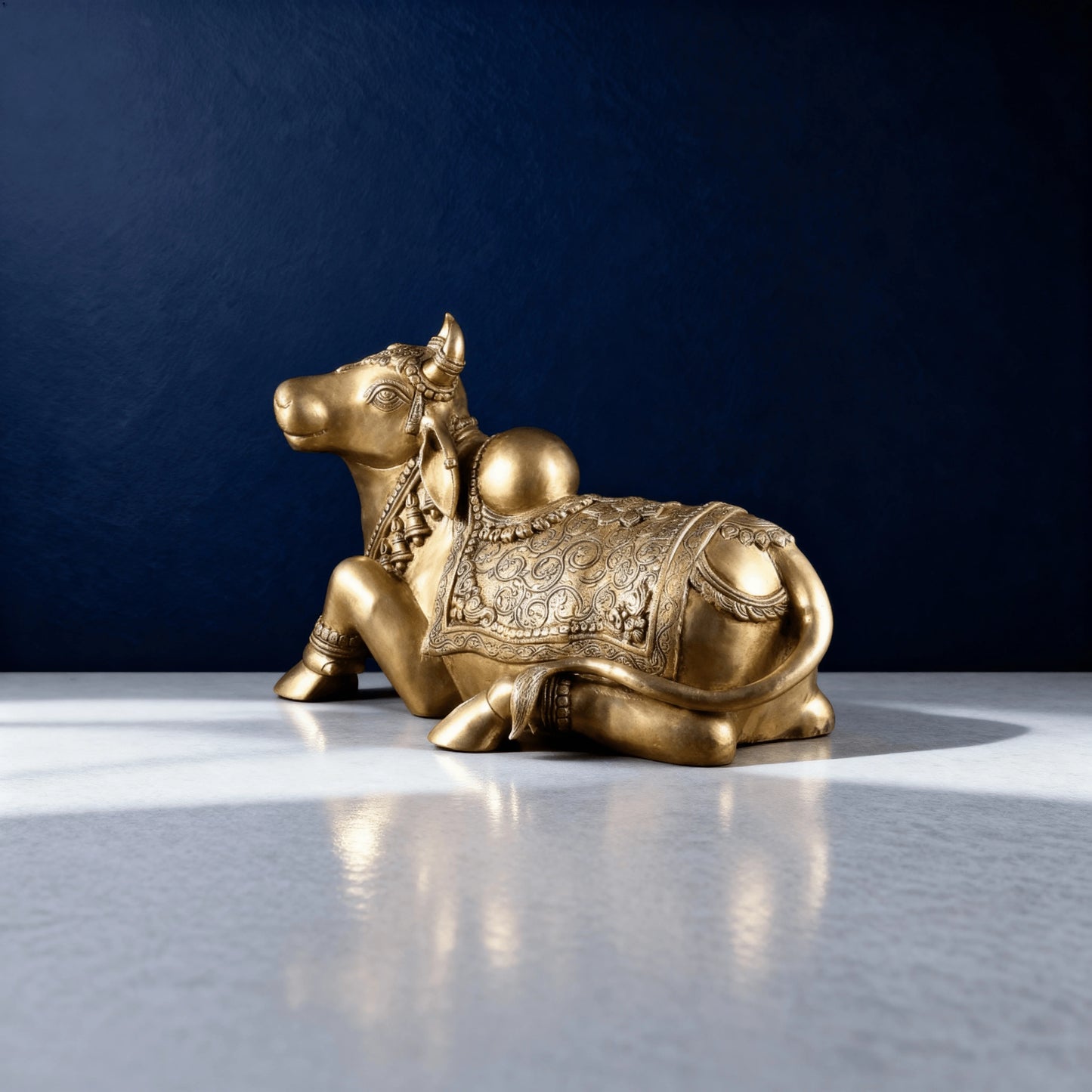 angled view of brass Nandi statue resting on a white surface, highlighting the curved tail and carved body patterns