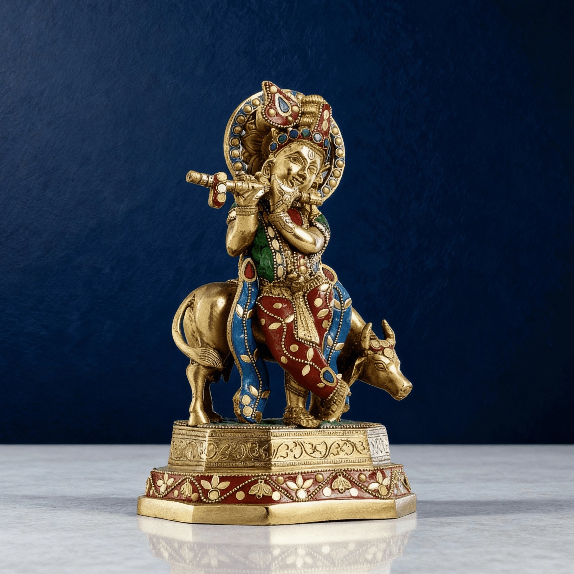 Artistic angled view of brass Krishna with cow idol decorated with multicolor stone inlay and ornate handcrafted patterns