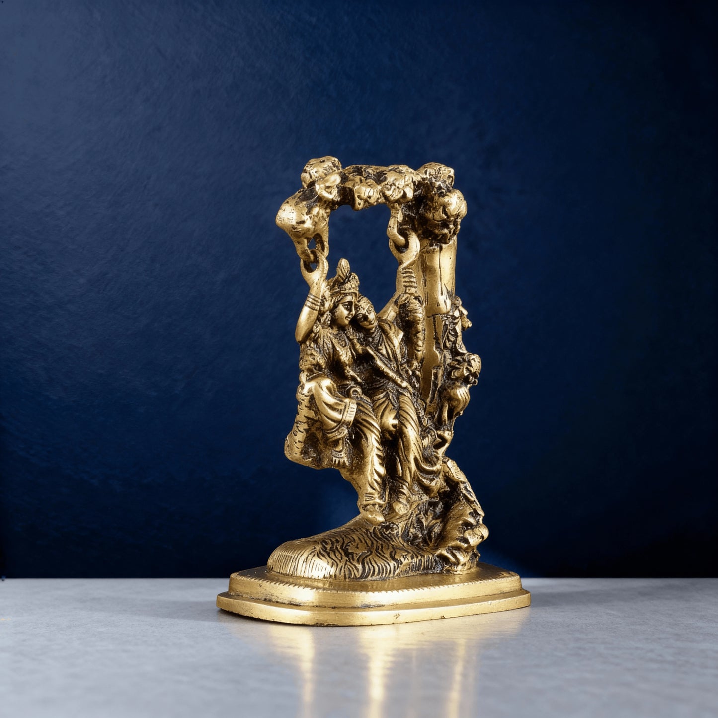 Side angle brass Radha Krishna swing idol with ornate tree frame, detailed handcrafted statue for spiritual home decor.